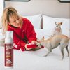 Woman in red sweater playing with a small dog on a bed next to a bottle of foaming product labeled 'Fresh & Foamy AF'