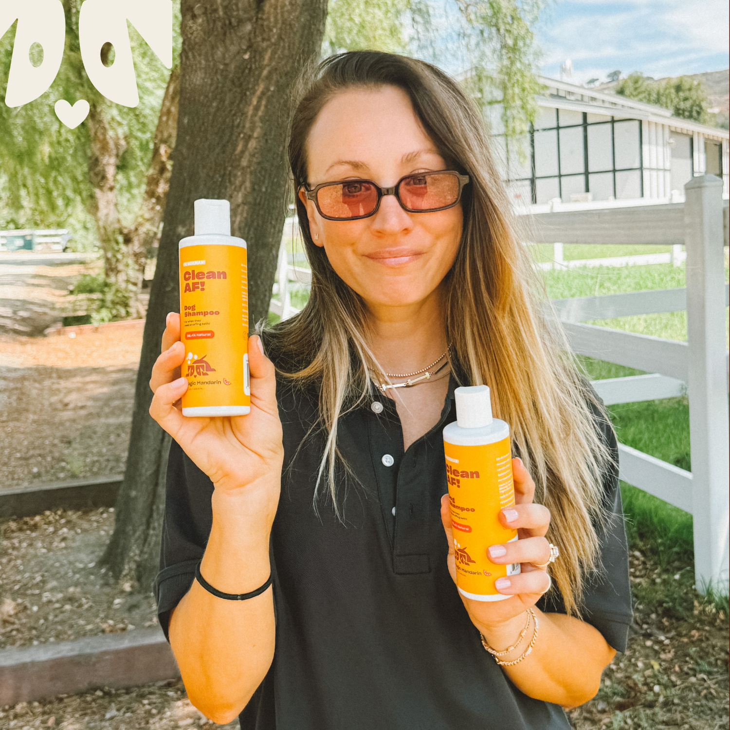 Woman smiling outdoors holding two bottled drinks labeled 'Clean AF'.