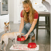 Woman feeding a small dog from a red Oh-riginal bowl in a kitchen setting