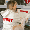 Kaley Cuoco wearing a jacket labeled 'PATIENT' holding a dog wearing a jacket labeled 'THERAPIST'