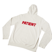 Back view of cream hoodie showcasing bold red PATIENT text on the back with white background