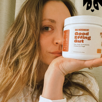 Kaley Cuoco holding a container labeled 'OH NORMAN! Good Effing Gut Pre, Post, & Probiotic Chews for Dogs'