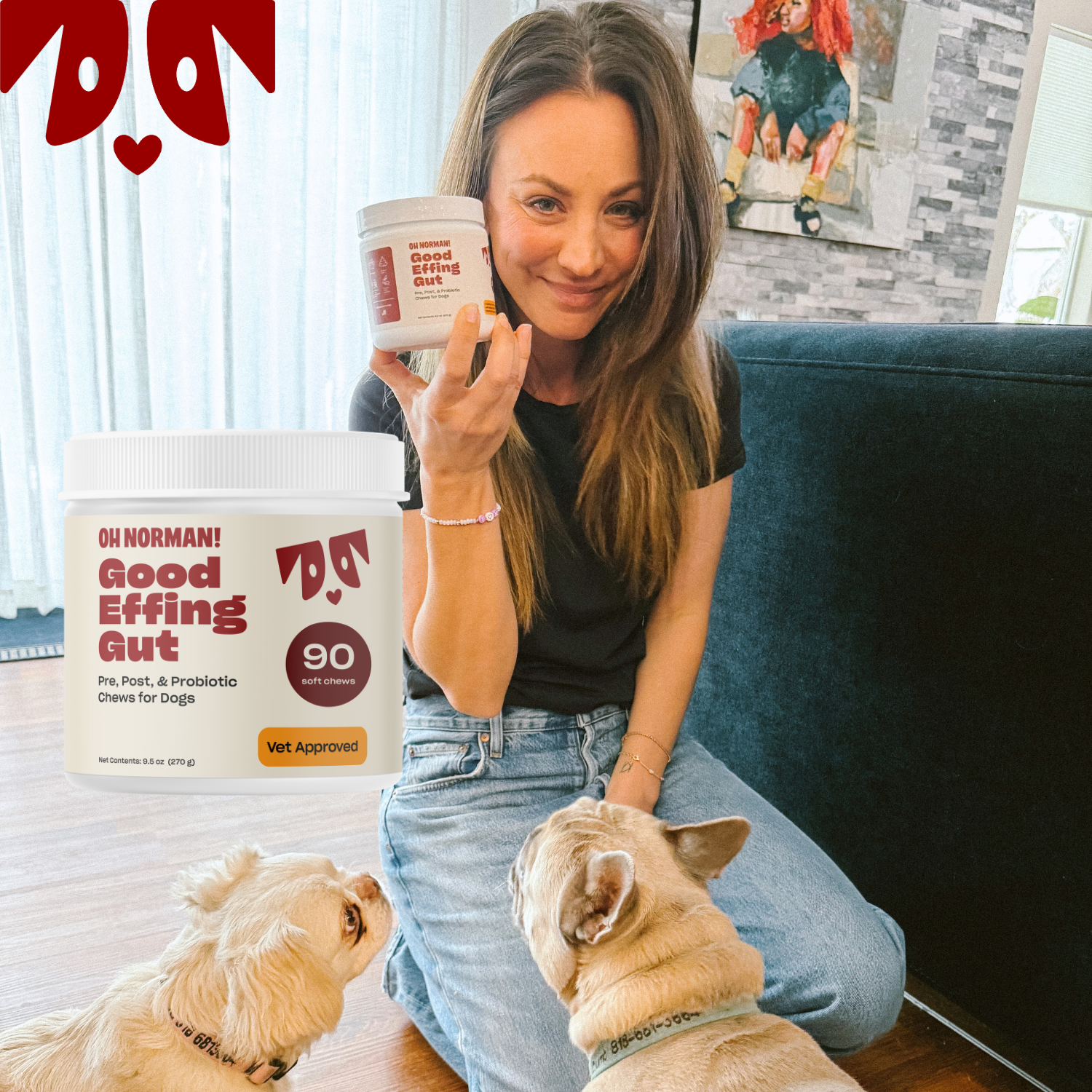 Actress Kaley Cuoco kneeling beside a couch holding a jar labeled Oh Norman Good Effing Gut 90 soft chews while two small dogs look up